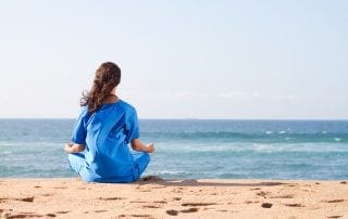 A nurse practicing self care, meditating on the beach after a hard day