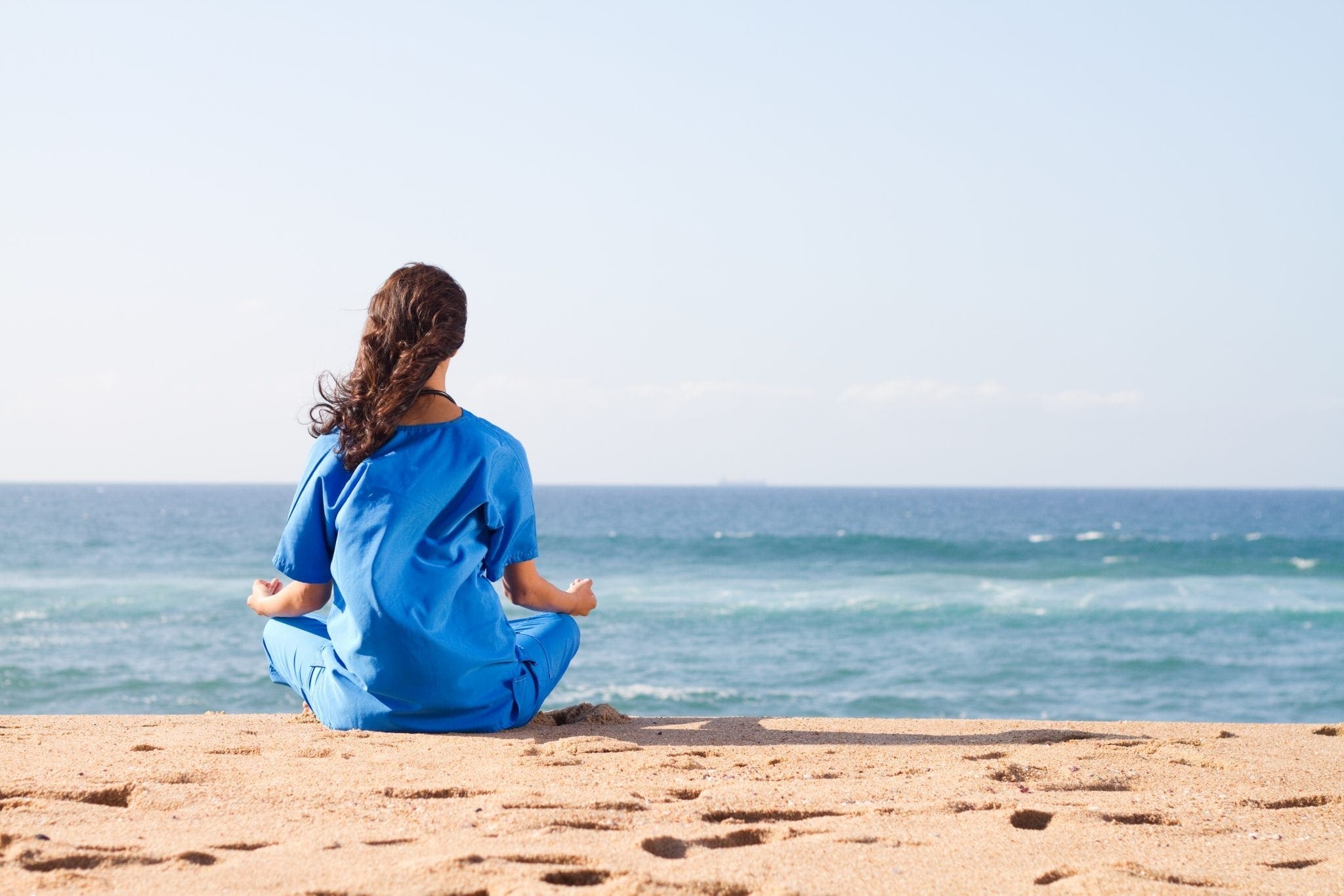 A nurse practicing self care, meditating on the beach after a hard day